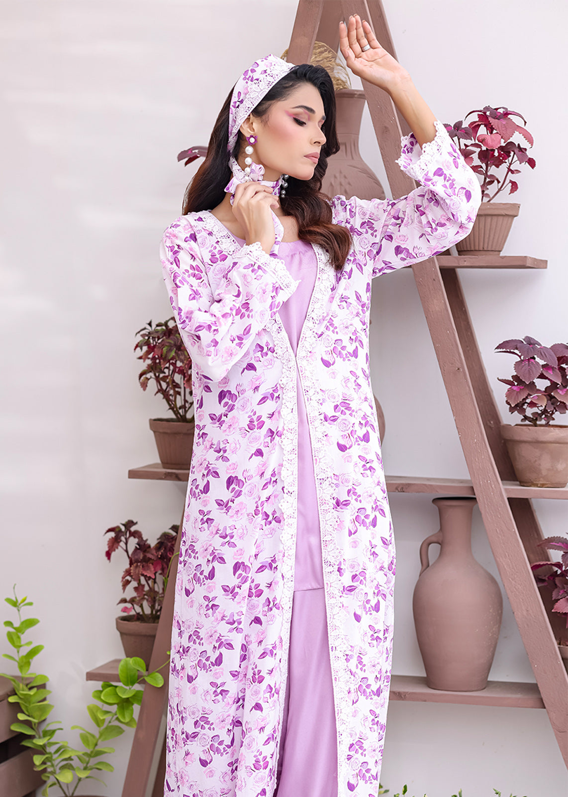 Woman wearing a long floral dress with a matching headscarf in a room with plants.