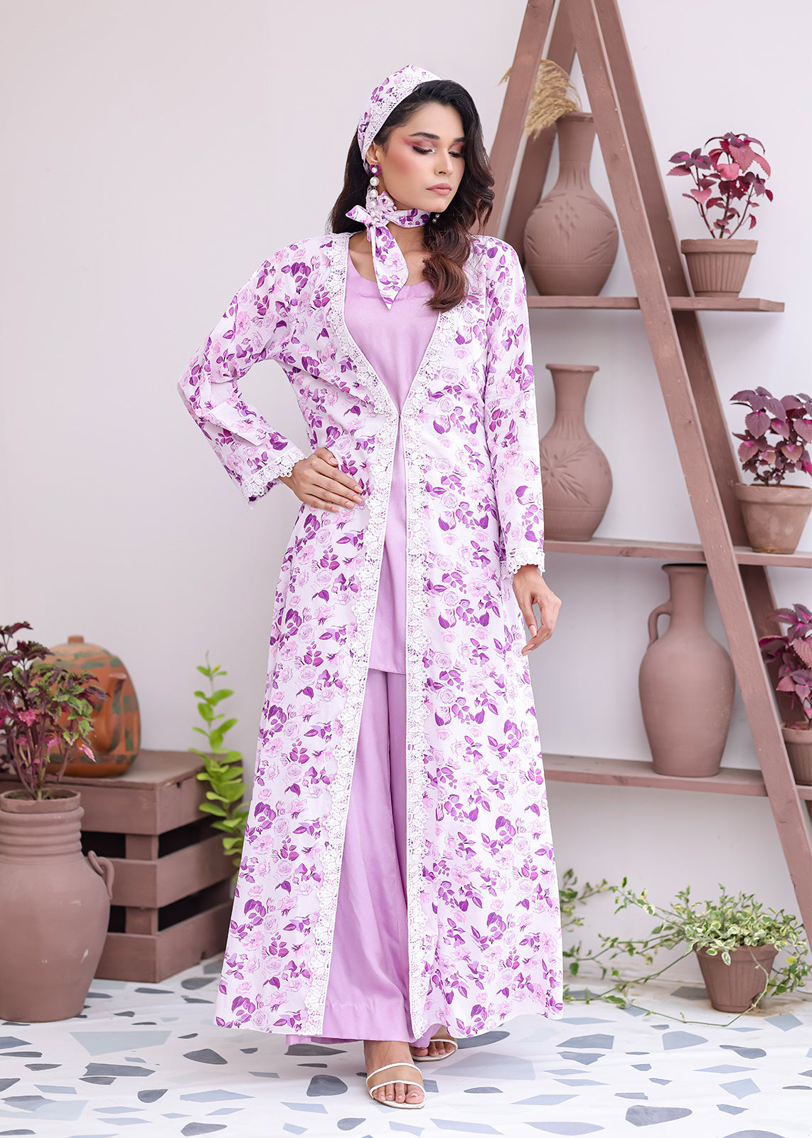 Woman wearing a floral dress and headscarf in a room with shelves and plants.